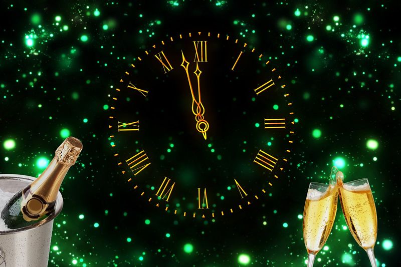 Große, beleuchtete Uhr kurz vor Mitternacht, Champagnerkühler mit Flasche und zwei angestoßene Gläser.