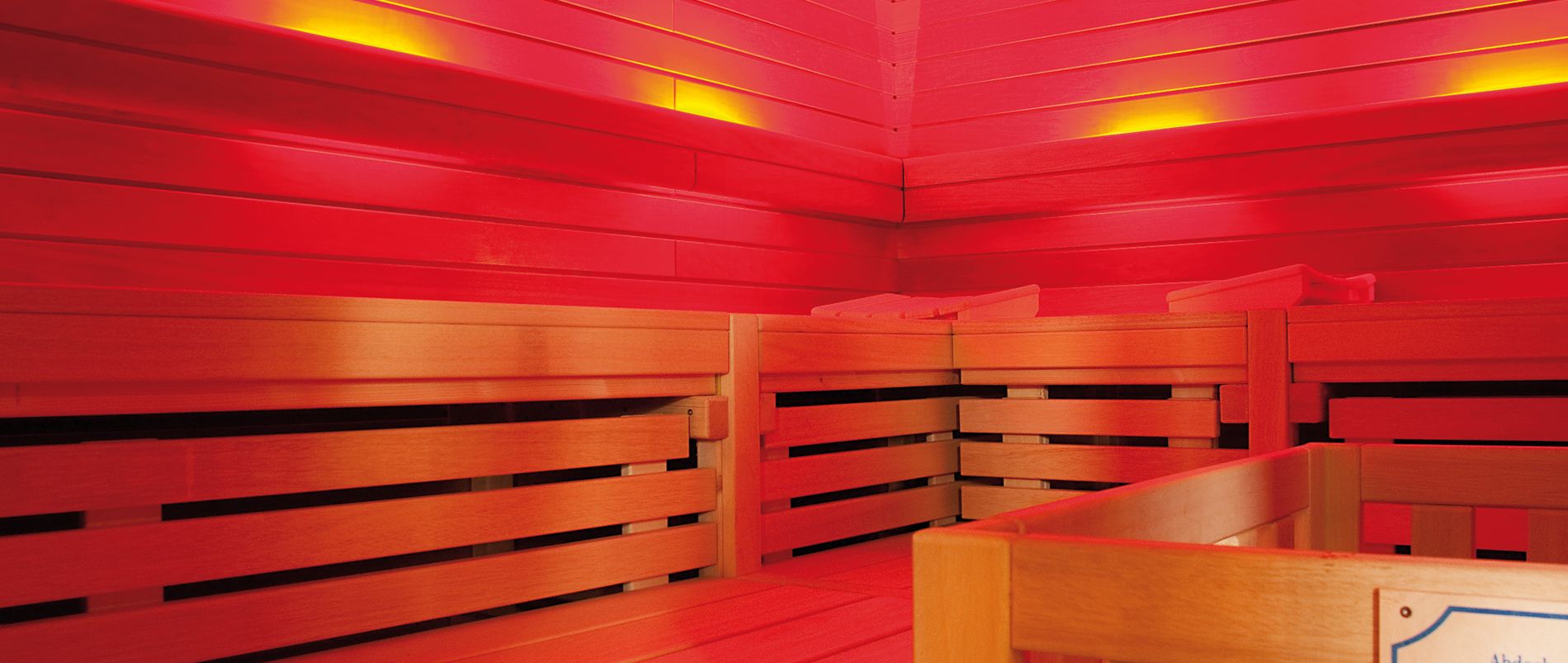 Innenansicht einer Sauna mit hölzernen Bänken und roter Beleuchtung