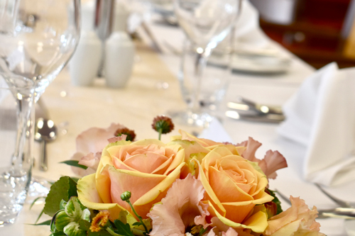 Elegant gedeckter Tisch mit Blumengesteck aus rosa und gelben Rosen