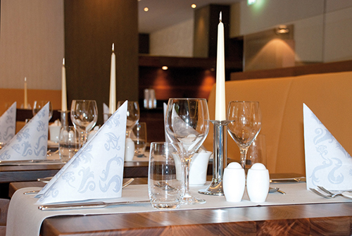 Eleganter Restauranttisch mit gefalteten Servietten, Kerzen und Gläsern eingedeckt.