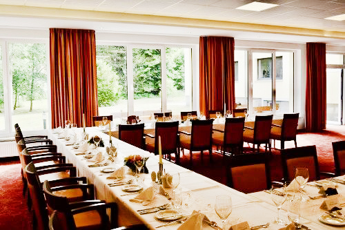 Festlich gedeckter Konferenztisch in einem großen Raum mit bodentiefen Fenstern.