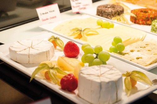 Ein Buffet mit verschiedenen Sorten Käse, darunter Camembert und Schnittkäse, dekoriert mit frischen Erdbeeren und Trauben.