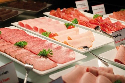 Tablett mit verschiedenen Wurst- und Schinkensorten, dekoriert mit Petersilie und Kirschtomaten.