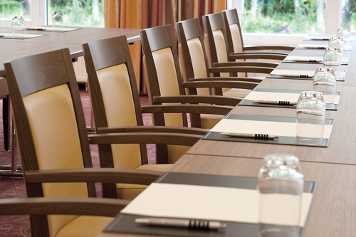 Ein Konferenzraum mit einer Reihe von leeren Stühlen und einem Tisch mit Schreibutensilien und Gläsern.