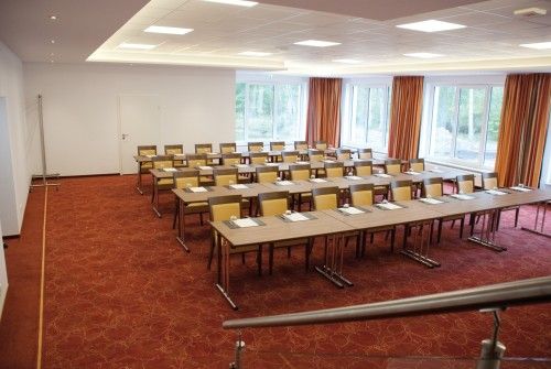 Konferenzraum mit Tischen und Stühlen in Reihen, rote Teppiche, große Fenster mit Vorhängen