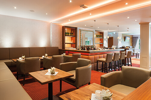 Moderner Lounge- und Barbereich mit Ledersesseln, Holztischen und einer gut bestückten Theke.