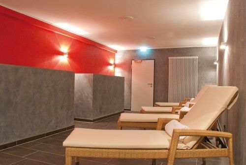 Ruheraum mit Liegestühlen, grauen Wänden und rot beleuchteten Akzenten.