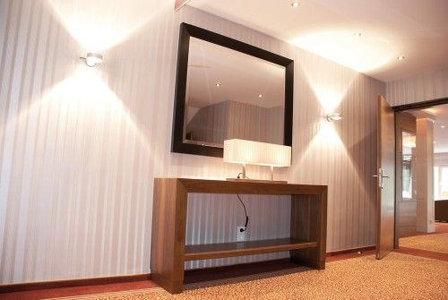 Moderner Flur mit Holzkonsole, großem Spiegel und Beleuchtung.