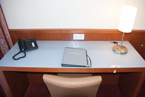Ein Hotelzimmer-Schreibtisch mit einem Telefon, einer Stehlampe und einer Mappe.