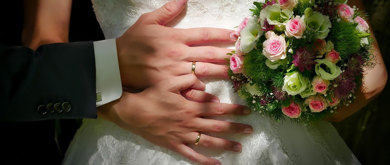 Nahaufnahme von Händen eines Hochzeitspaares mit Blumenstrauß
